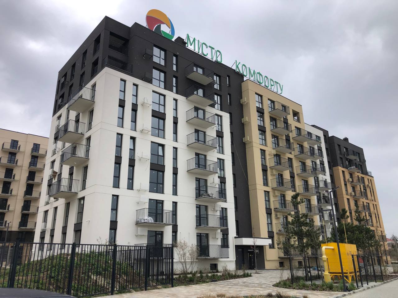 Modern apartment complex with white and beige façades, black accents, and repeating balconies.