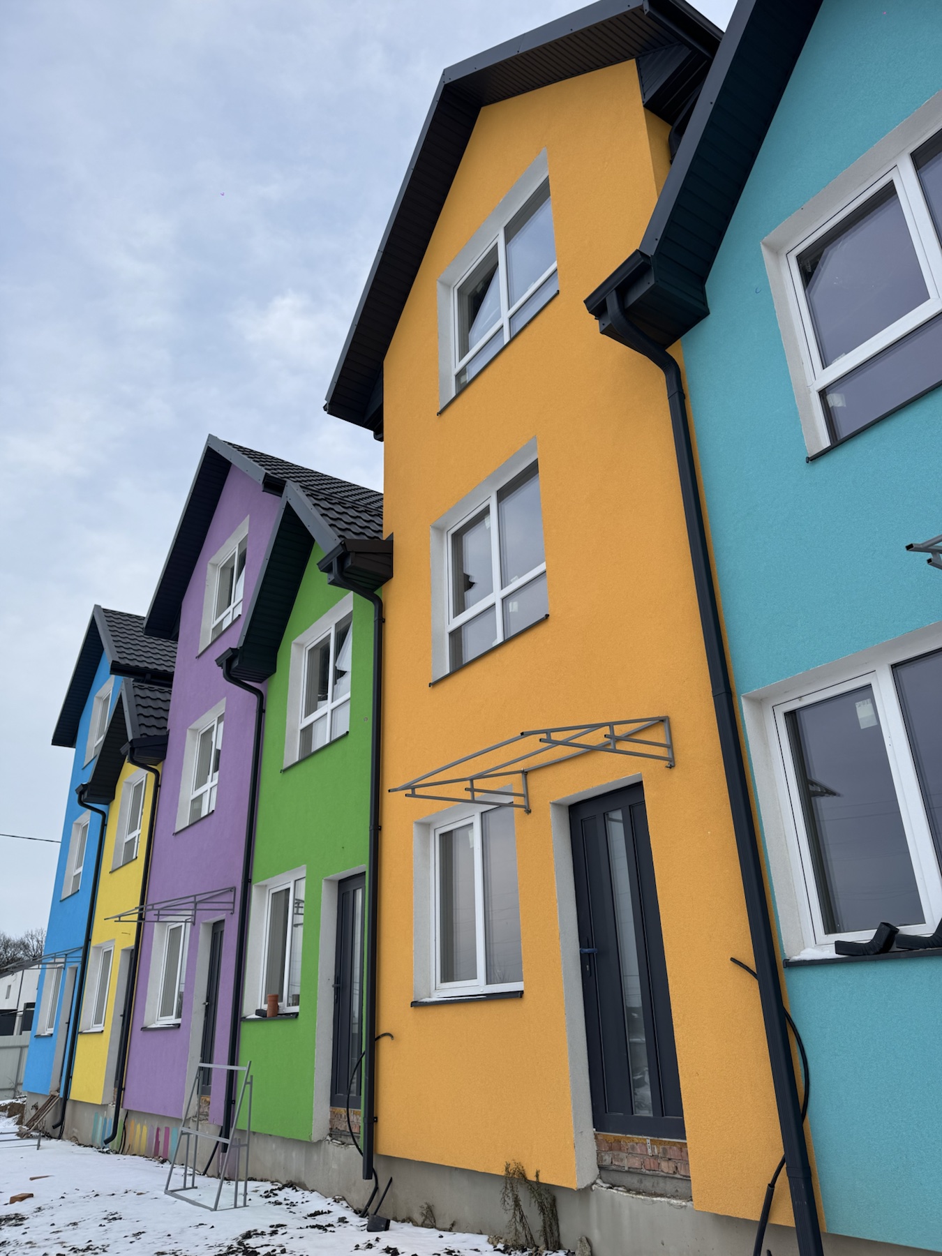 Row of brightly colored houses in blue, yellow, purple, green, and turquoise along a snowy street, viewed from a low angle.