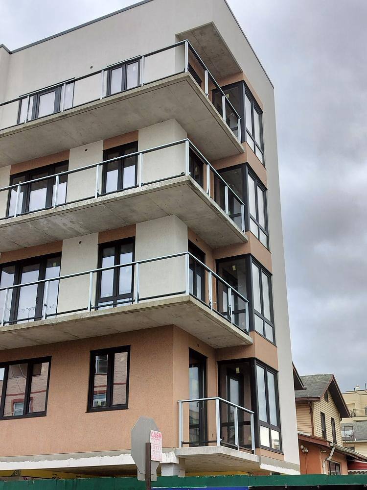 Modern multi-story apartment building with glass balcony railings and beige exterior.